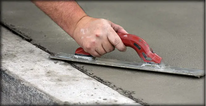 A person using a red tool to level concrete.