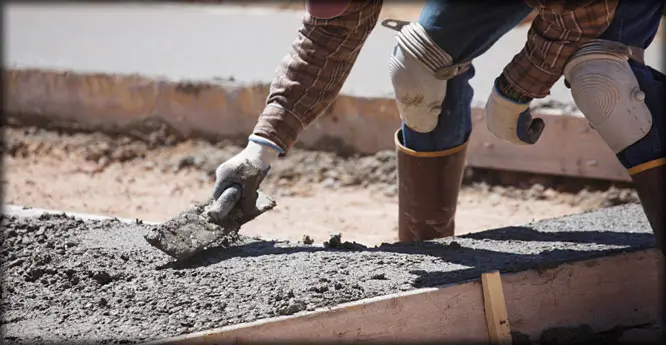 A person in white gloves and black boots is pouring cement.