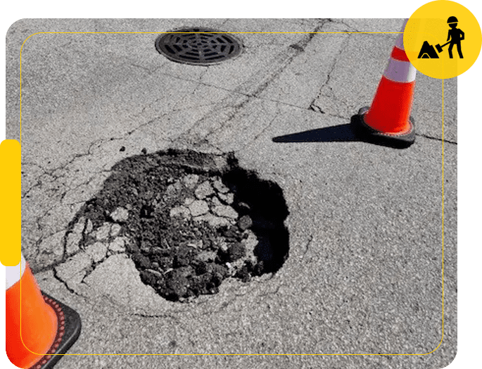 A hole in the ground with a yellow traffic cone next to it.